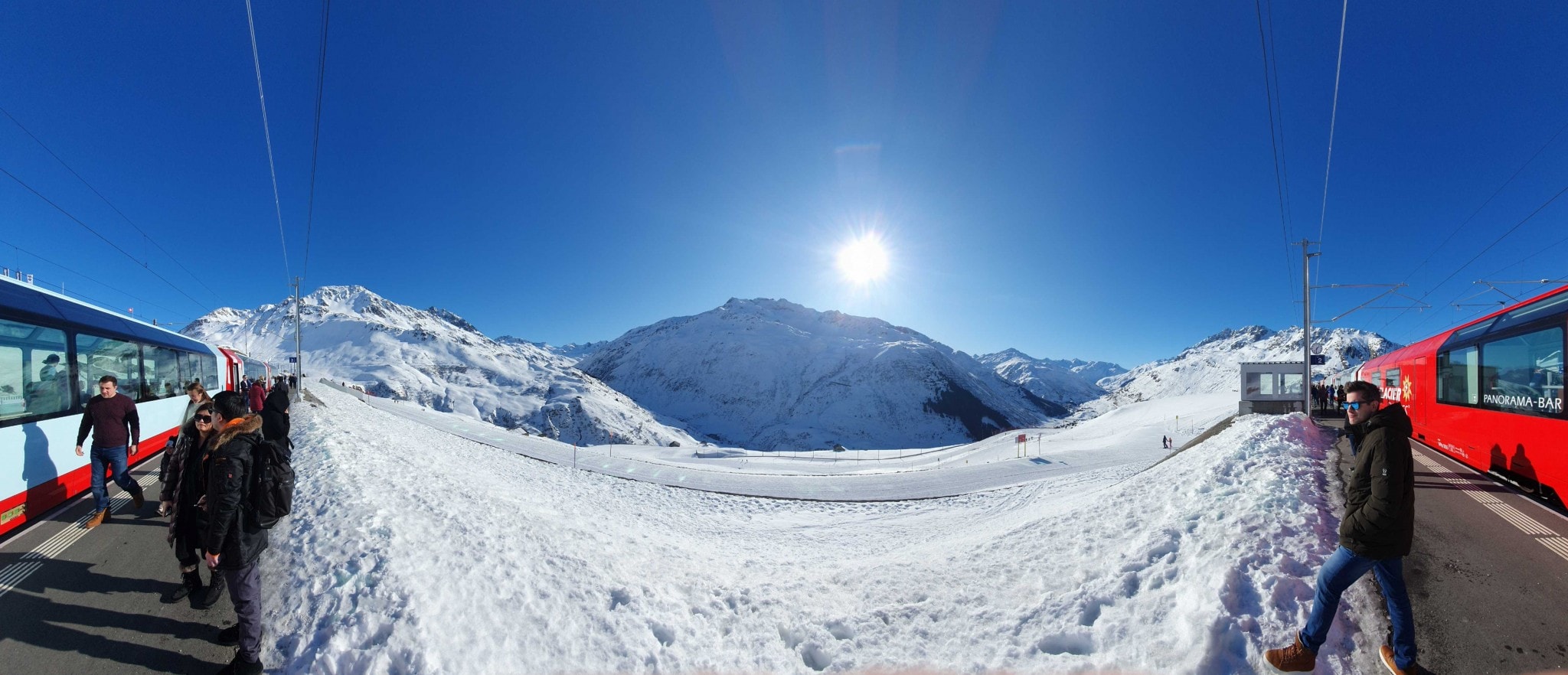 Panorama photo of train, people and view of sun, snow and mountains