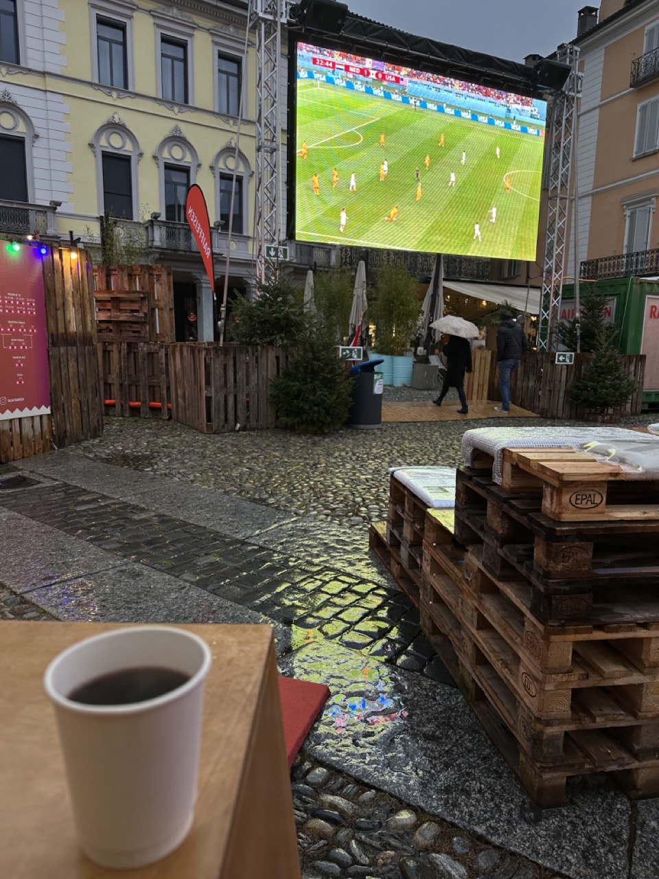 Blick auf den Public-Viewing-Screen am Weihnachtsmarkt bei Nacht mit einem Becher Glühwein