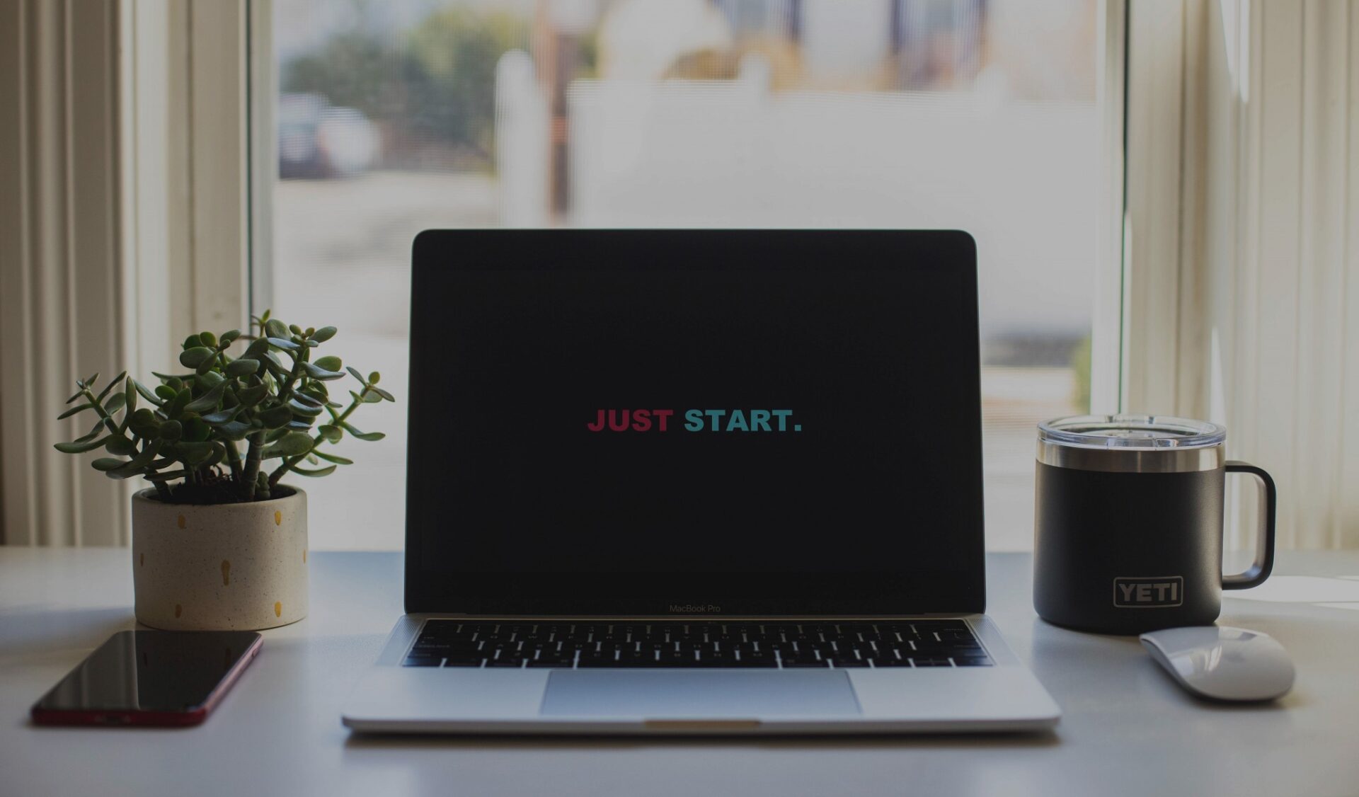 An open laptop with the words "Just Start" on the screen.