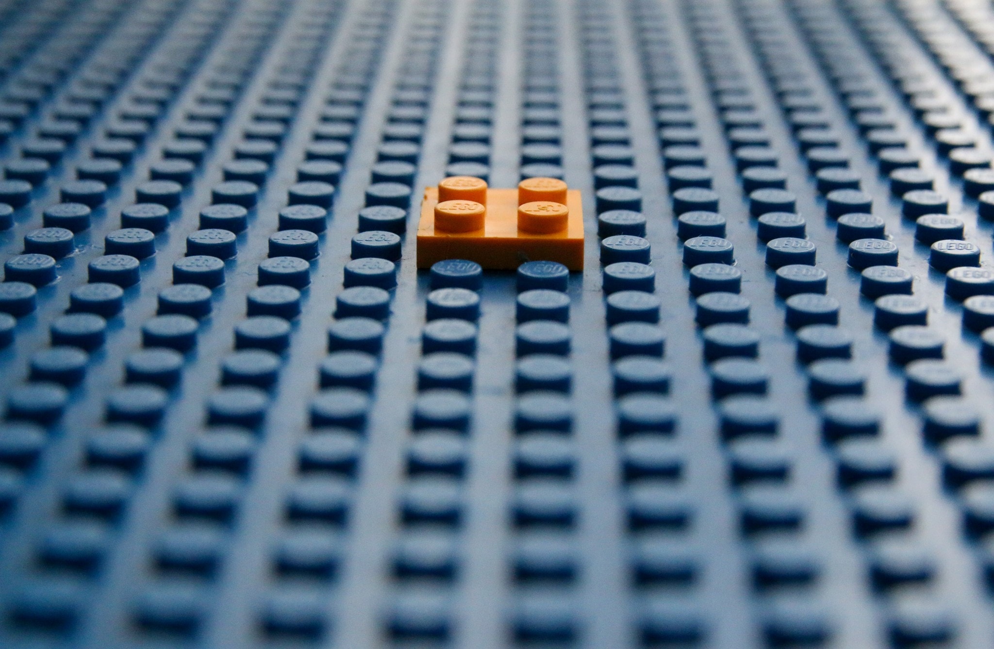 A single orange Lego brick on a large blue surface