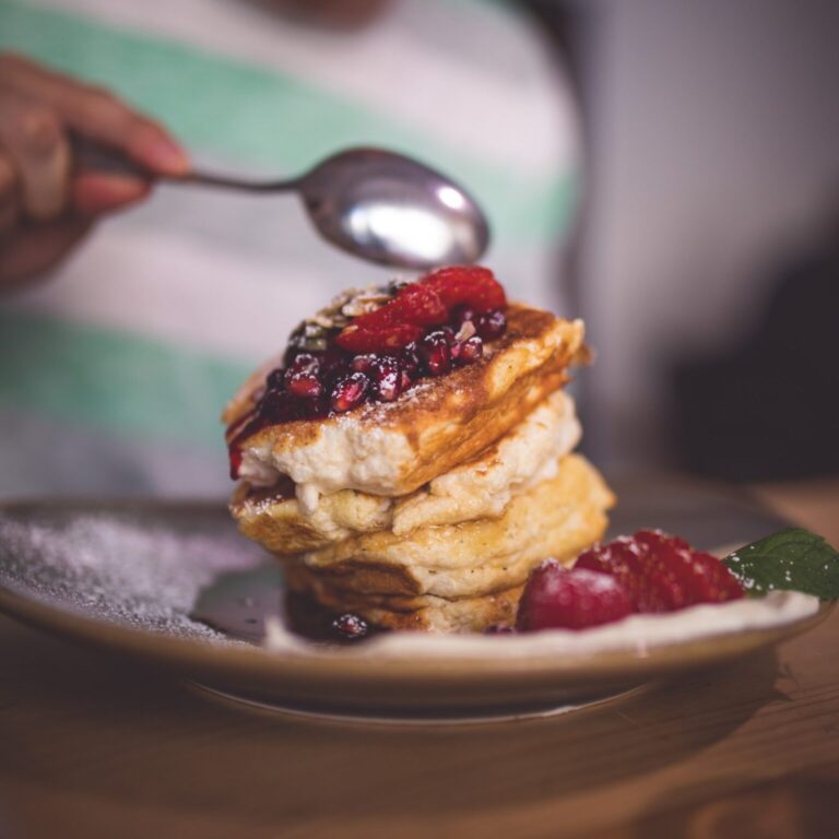 Foto von fluffigen Pancakes, welche auf einander gestapelt sind und mit Früchten garniert