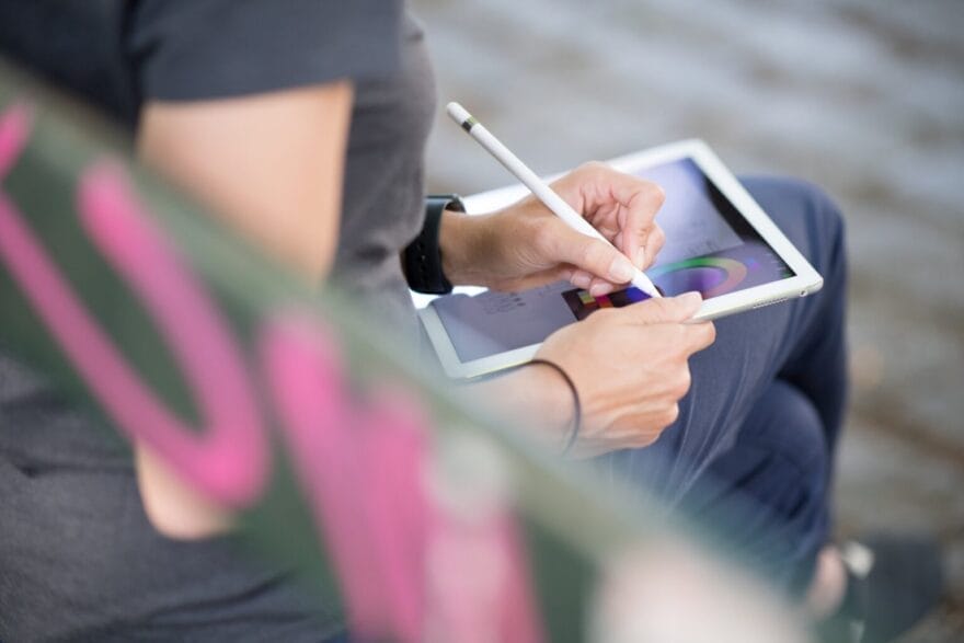 Karin is drawing concepts on her iPad and sitting outdoors on a bench.