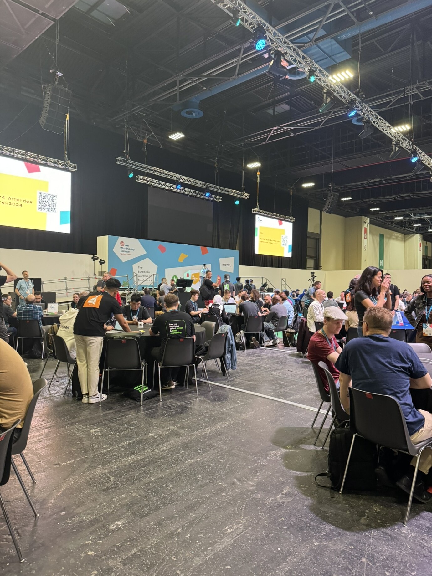 Foto vom Contributor Day, mit vielen Menschen drauf an Tischen verteilt am arbeiten.