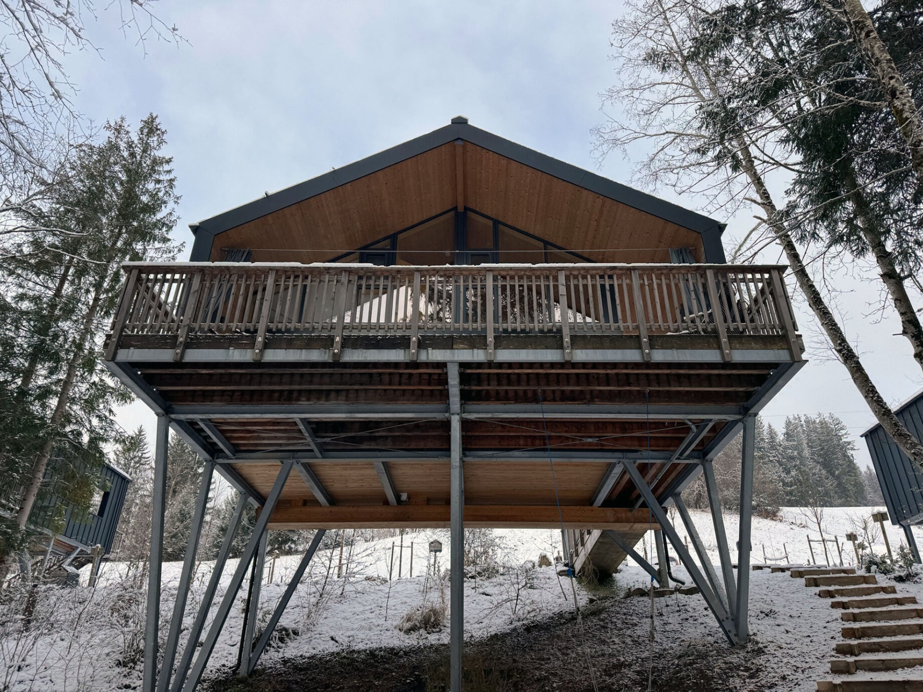 Ein Chalet auf Stelzen in winterlicher Landschaft, umgeben von Schnee und Bäumen, mit einer beleuchteten Terrasse, die Gemütlichkeit ausstrahlt.