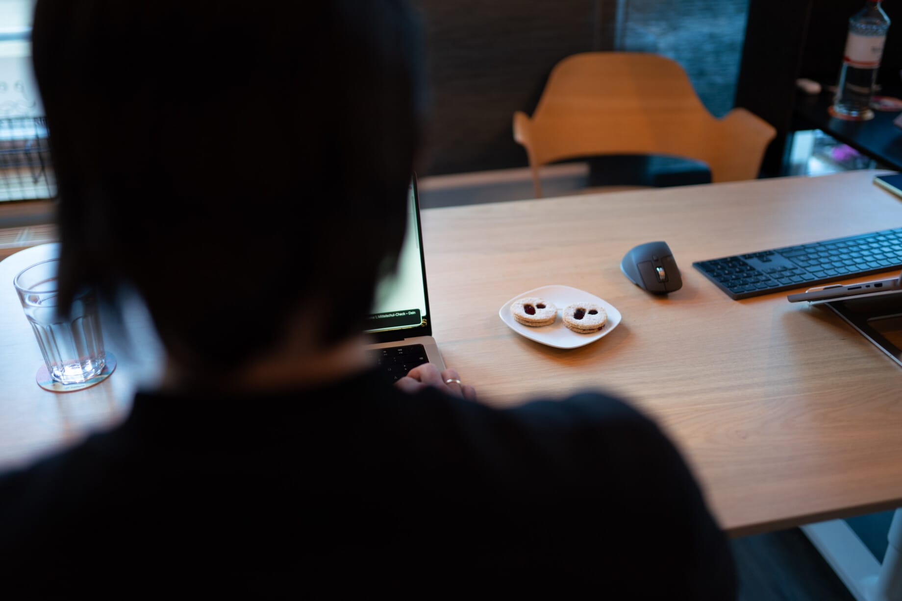 Person working on a laptop at a wooden desk; a mouse, keyboard, and a plate with two required branded cookies are visible on the table.