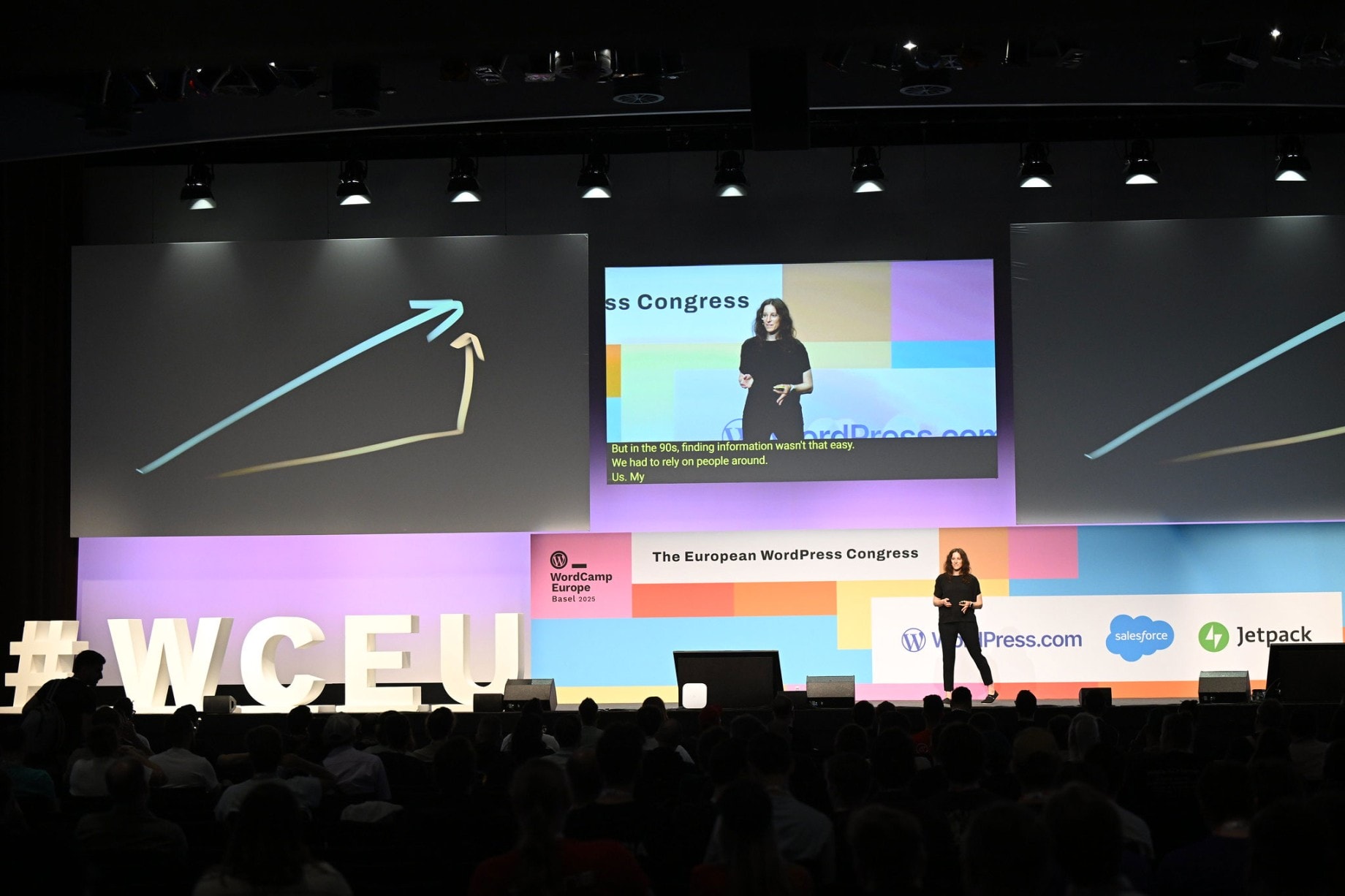 WordCamp Europe 2025: Karin as speaker on stage with geometric graphics and spectators in the audience